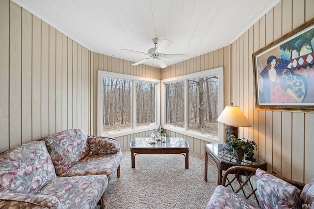 carpeted living area with ceiling fan and wood walls