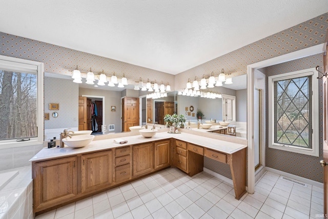 bathroom with tiled bath, wallpapered walls, baseboards, double vanity, and a sink