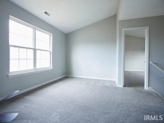 carpeted spare room featuring vaulted ceiling, baseboards, and visible vents