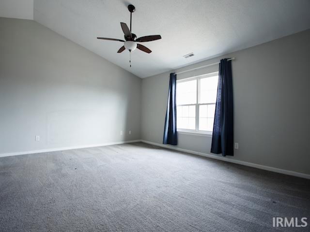 carpeted empty room with vaulted ceiling, visible vents, baseboards, and ceiling fan