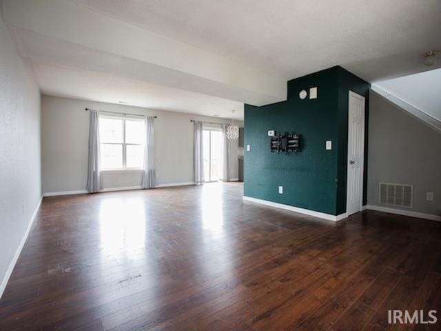 unfurnished living room with baseboards, wood finished floors, visible vents, and a chandelier