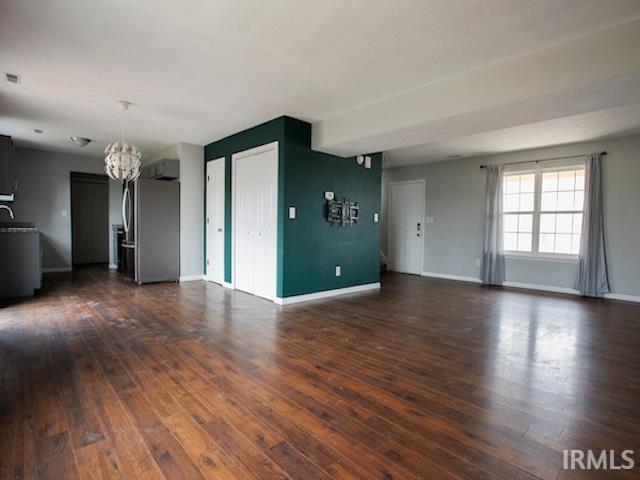 unfurnished living room featuring a chandelier, dark wood-style floors, and baseboards