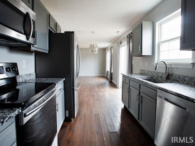 kitchen featuring a chandelier, light stone counters, dark wood-style floors, stainless steel appliances, and a sink