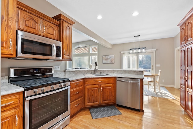 kitchen with brown cabinetry, a peninsula, light wood-style flooring, a sink, and stainless steel appliances