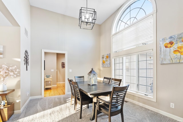 dining space featuring carpet, an inviting chandelier, a towering ceiling, and a healthy amount of sunlight