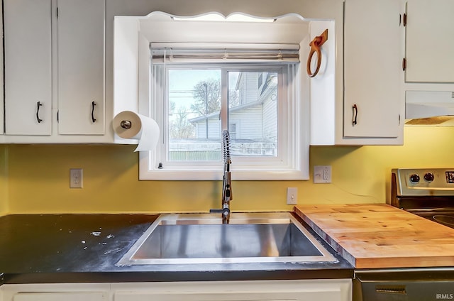 kitchen with ventilation hood, stainless steel range with electric cooktop, a sink, white cabinets, and wood counters