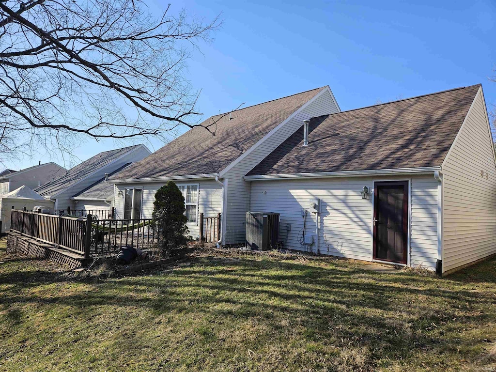 back of property with a wooden deck, a lawn, and roof with shingles