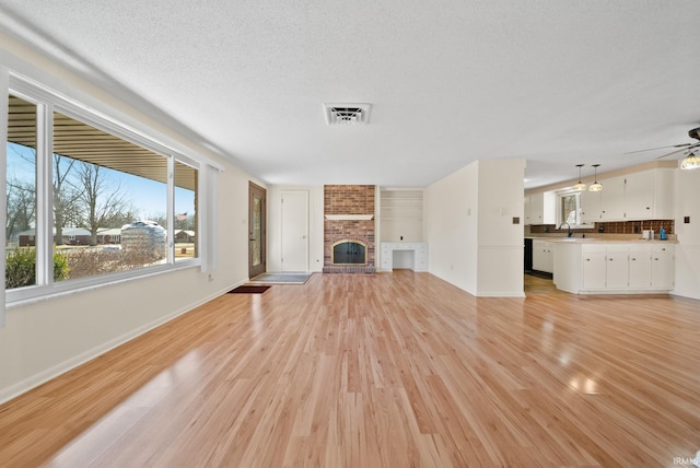 unfurnished living room featuring visible vents, light wood-style flooring, a ceiling fan, a textured ceiling, and a fireplace