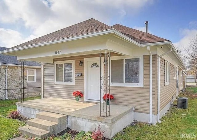 bungalow-style home with a porch, central AC, and roof with shingles