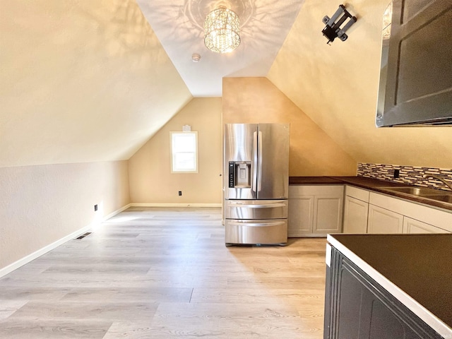 kitchen featuring dark countertops, stainless steel fridge with ice dispenser, vaulted ceiling, light wood-style floors, and a sink