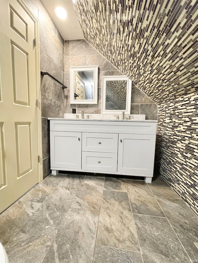 full bathroom featuring a tile shower, tile walls, vanity, and vaulted ceiling