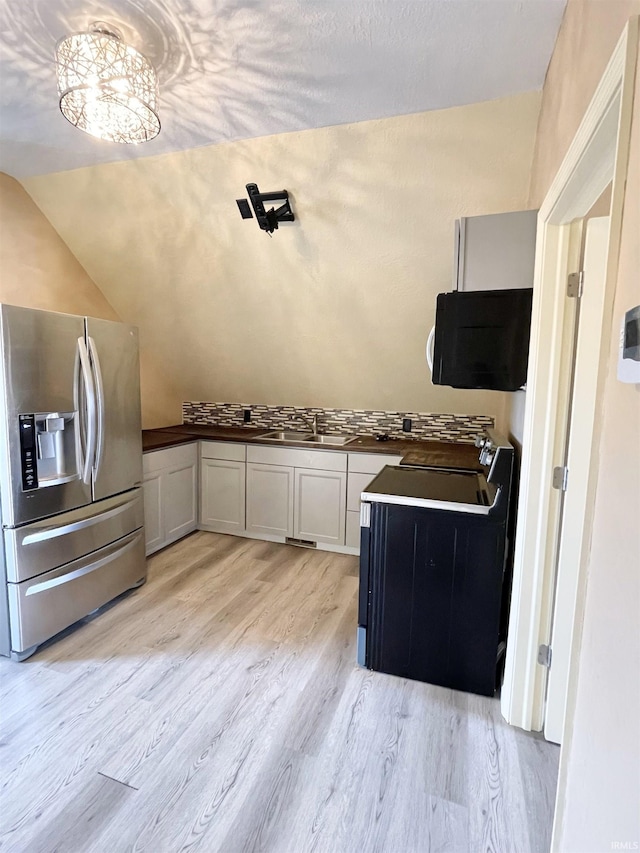 kitchen featuring light wood-style flooring, stainless steel refrigerator with ice dispenser, dark countertops, electric range oven, and lofted ceiling