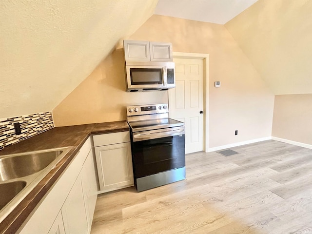 kitchen with light wood-style floors, stainless steel appliances, dark countertops, and backsplash