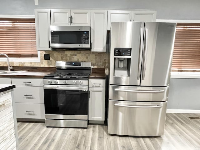 kitchen with decorative backsplash, light wood-style flooring, appliances with stainless steel finishes, and a sink