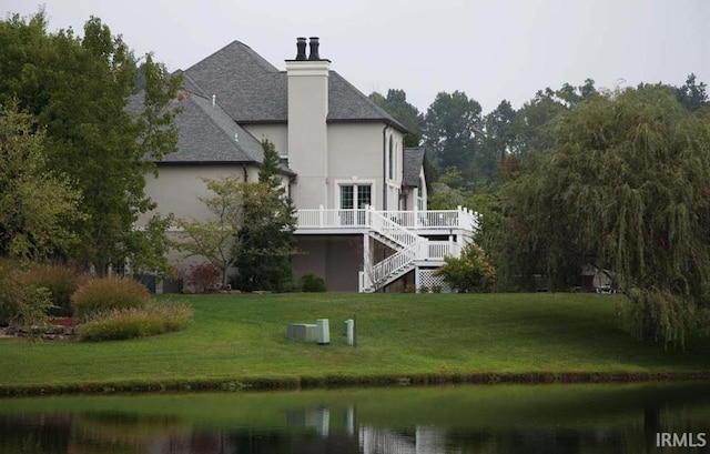 rear view of property with stairway, a deck with water view, roof with shingles, a yard, and stucco siding