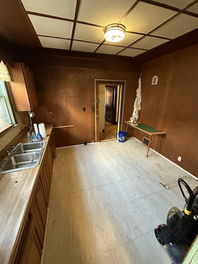 kitchen featuring wooden walls, brown cabinets, light countertops, and a sink