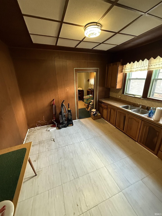 kitchen featuring light countertops, brown cabinetry, wood walls, and a sink