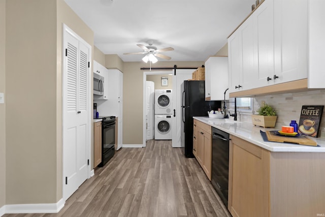 kitchen with light countertops, a barn door, stacked washer and dryer, black appliances, and a ceiling fan