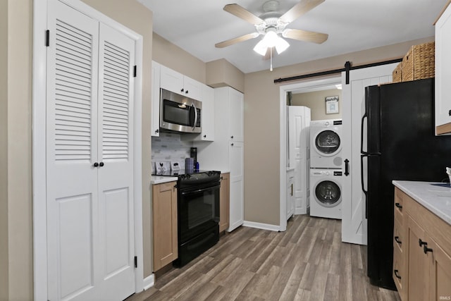 kitchen with wood finished floors, ceiling fan, black appliances, a barn door, and stacked washer / dryer