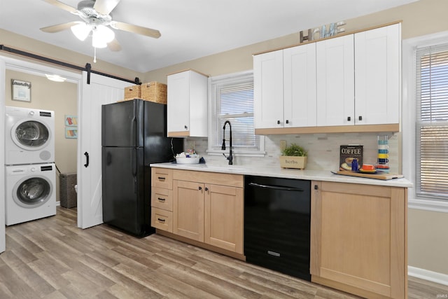 kitchen featuring a healthy amount of sunlight, light wood-type flooring, stacked washing maching and dryer, black appliances, and a sink