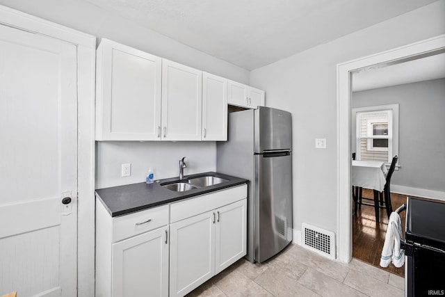 kitchen with visible vents, a sink, dark countertops, white cabinetry, and freestanding refrigerator