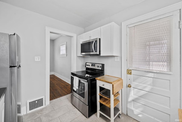 kitchen with visible vents, baseboards, light tile patterned floors, white cabinets, and stainless steel appliances