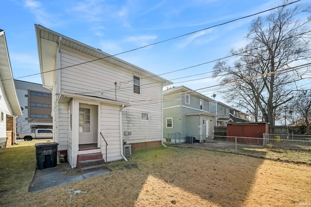 back of house featuring entry steps, central air condition unit, fence, and a lawn