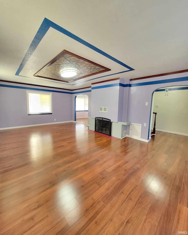 unfurnished living room with wood finished floors, visible vents, arched walkways, and ornamental molding