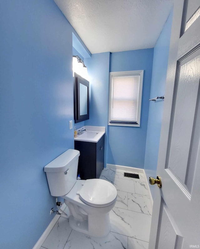 half bathroom with baseboards, toilet, vanity, marble finish floor, and a textured ceiling