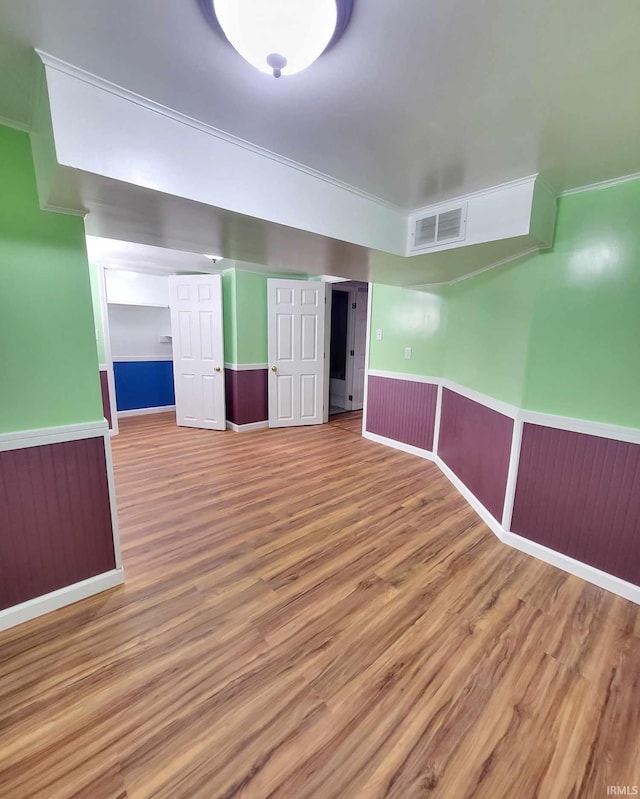 spare room featuring a wainscoted wall, visible vents, wood finished floors, and ornamental molding