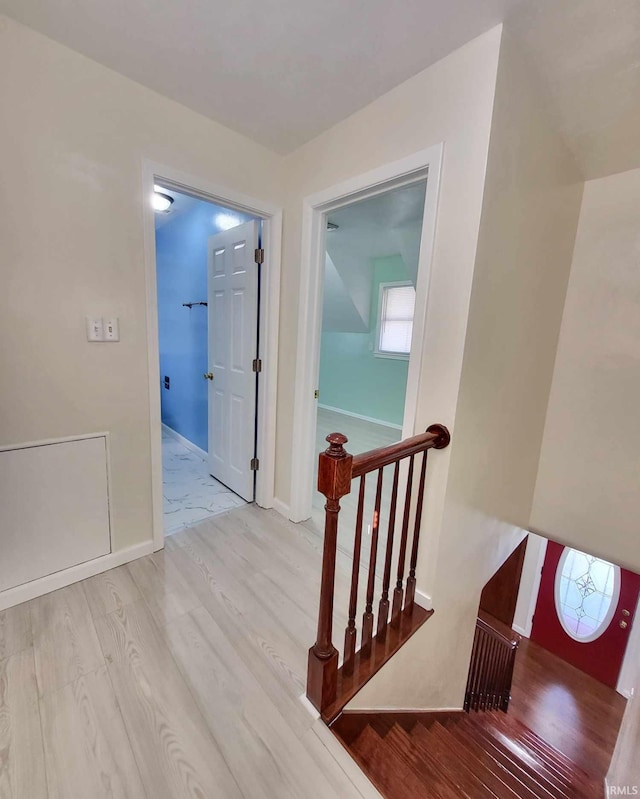 hallway with an upstairs landing, baseboards, and wood finished floors