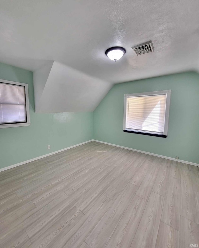 additional living space with wood finished floors, baseboards, visible vents, lofted ceiling, and a textured ceiling