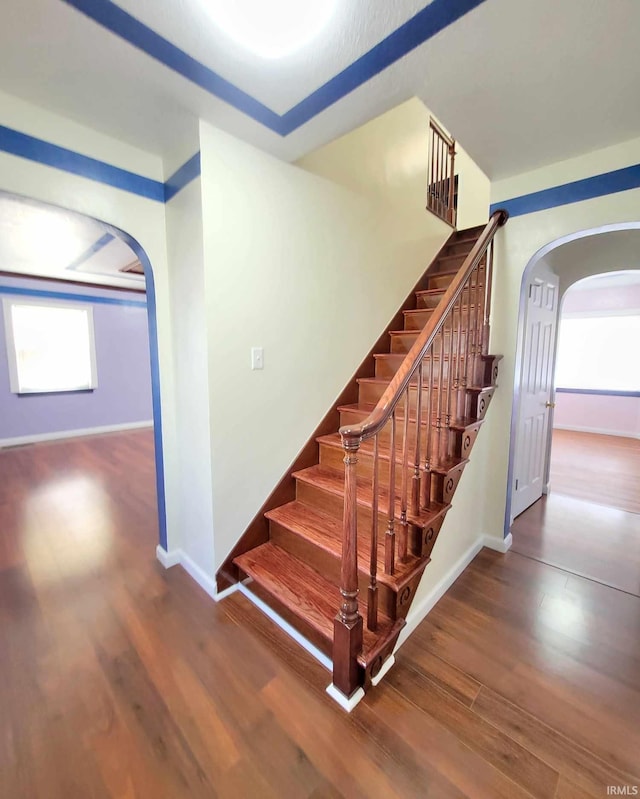 stairs with arched walkways, baseboards, and wood finished floors