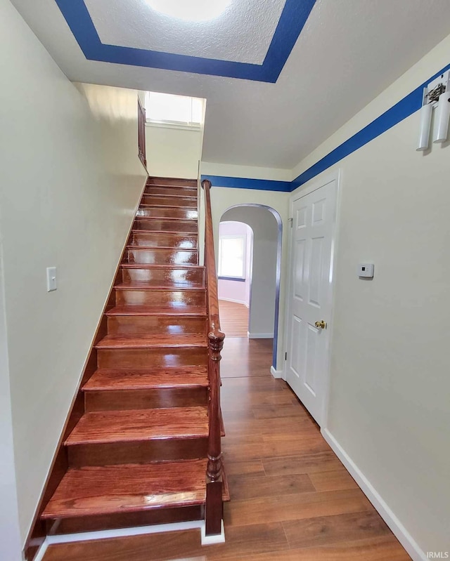 stairway with a textured ceiling, wood finished floors, arched walkways, and baseboards