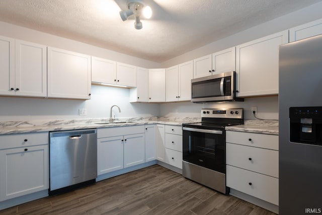 kitchen with a sink, light stone countertops, stainless steel appliances, white cabinetry, and dark wood-style flooring