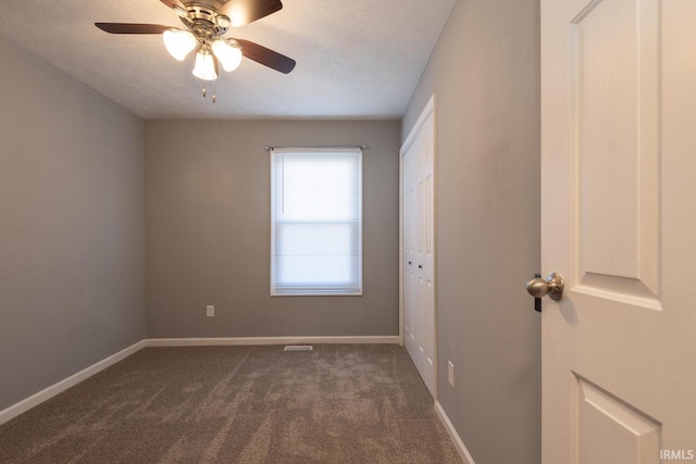 spare room featuring a textured ceiling, baseboards, dark colored carpet, and ceiling fan