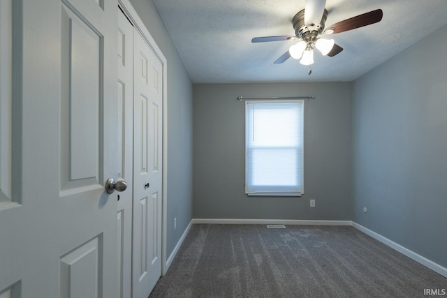 unfurnished bedroom featuring a closet, dark carpet, a textured ceiling, and baseboards