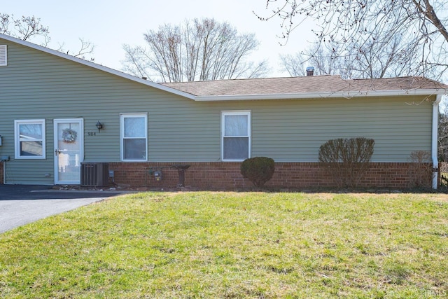 view of front of property with a front yard, central AC unit, and brick siding