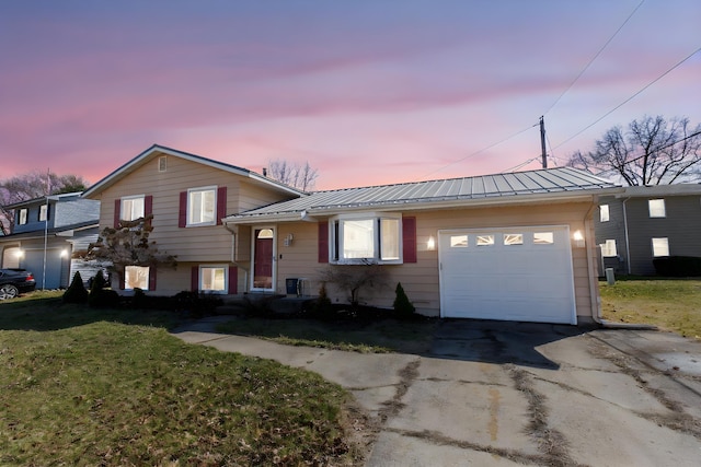 tri-level home featuring a front lawn, concrete driveway, metal roof, a garage, and a standing seam roof