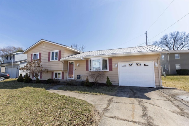 split level home featuring a front yard, a standing seam roof, concrete driveway, a garage, and metal roof