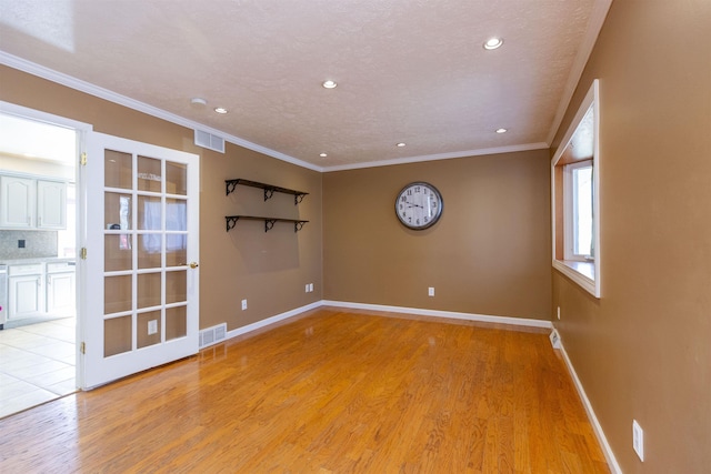 unfurnished room featuring light wood finished floors, visible vents, crown molding, and baseboards