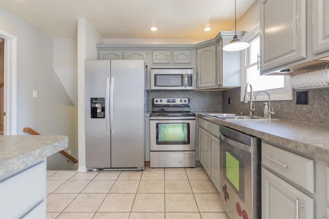 kitchen featuring tasteful backsplash, light tile patterned floors, gray cabinets, stainless steel appliances, and a sink