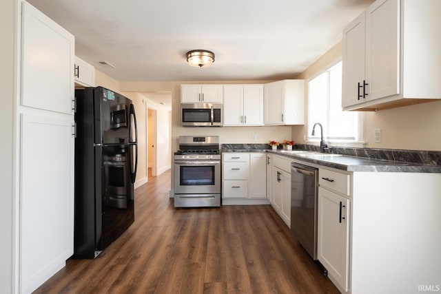 kitchen featuring a sink, dark countertops, dark wood-style floors, white cabinetry, and appliances with stainless steel finishes