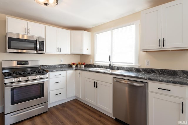 kitchen with a sink, dark wood-type flooring, white cabinets, appliances with stainless steel finishes, and dark countertops