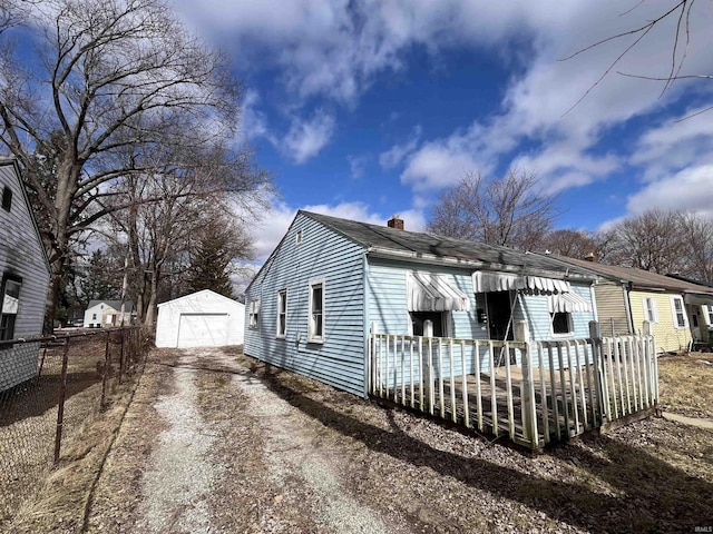 exterior space featuring dirt driveway, fence, an outdoor structure, a garage, and a chimney