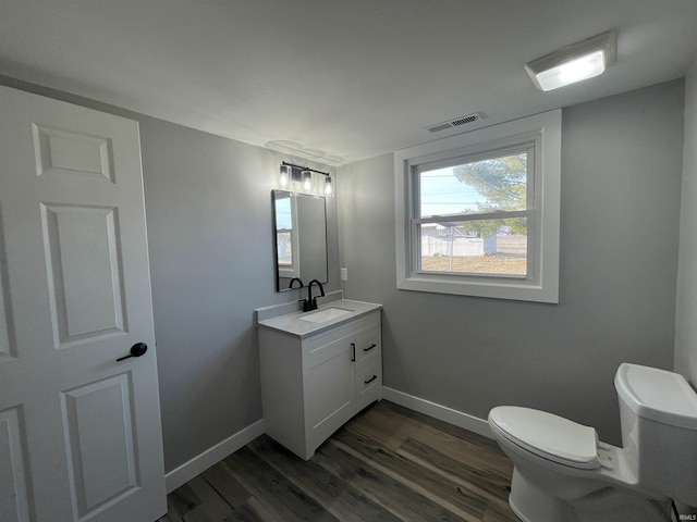 half bath with visible vents, toilet, baseboards, and wood finished floors