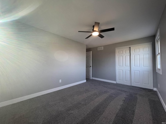 unfurnished bedroom with visible vents, dark carpet, a closet, baseboards, and ceiling fan