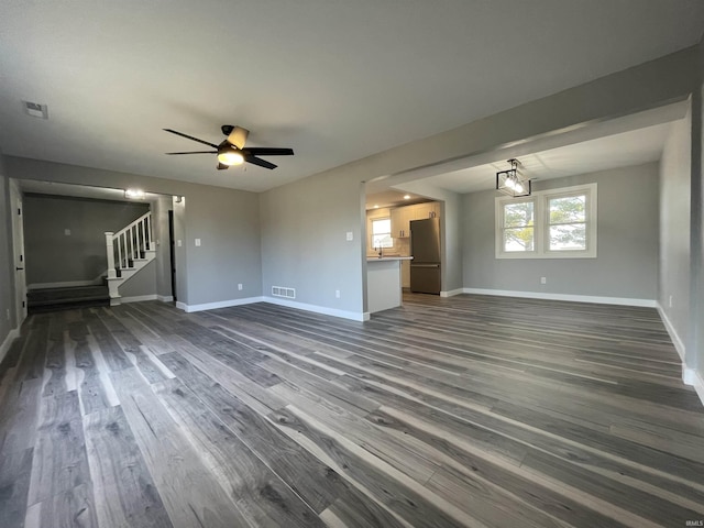 unfurnished living room with a ceiling fan, visible vents, baseboards, dark wood-style flooring, and stairs