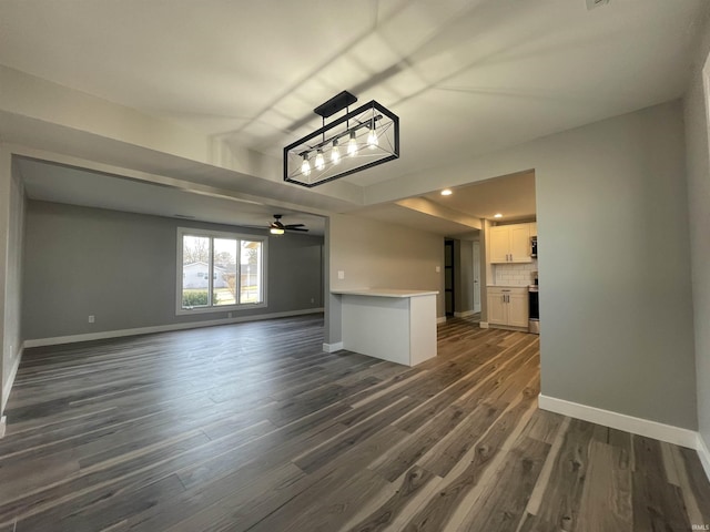 unfurnished living room featuring dark wood-type flooring, a ceiling fan, and baseboards