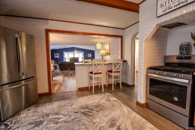 kitchen featuring brick wall, beamed ceiling, a breakfast bar, appliances with stainless steel finishes, and wood finished floors